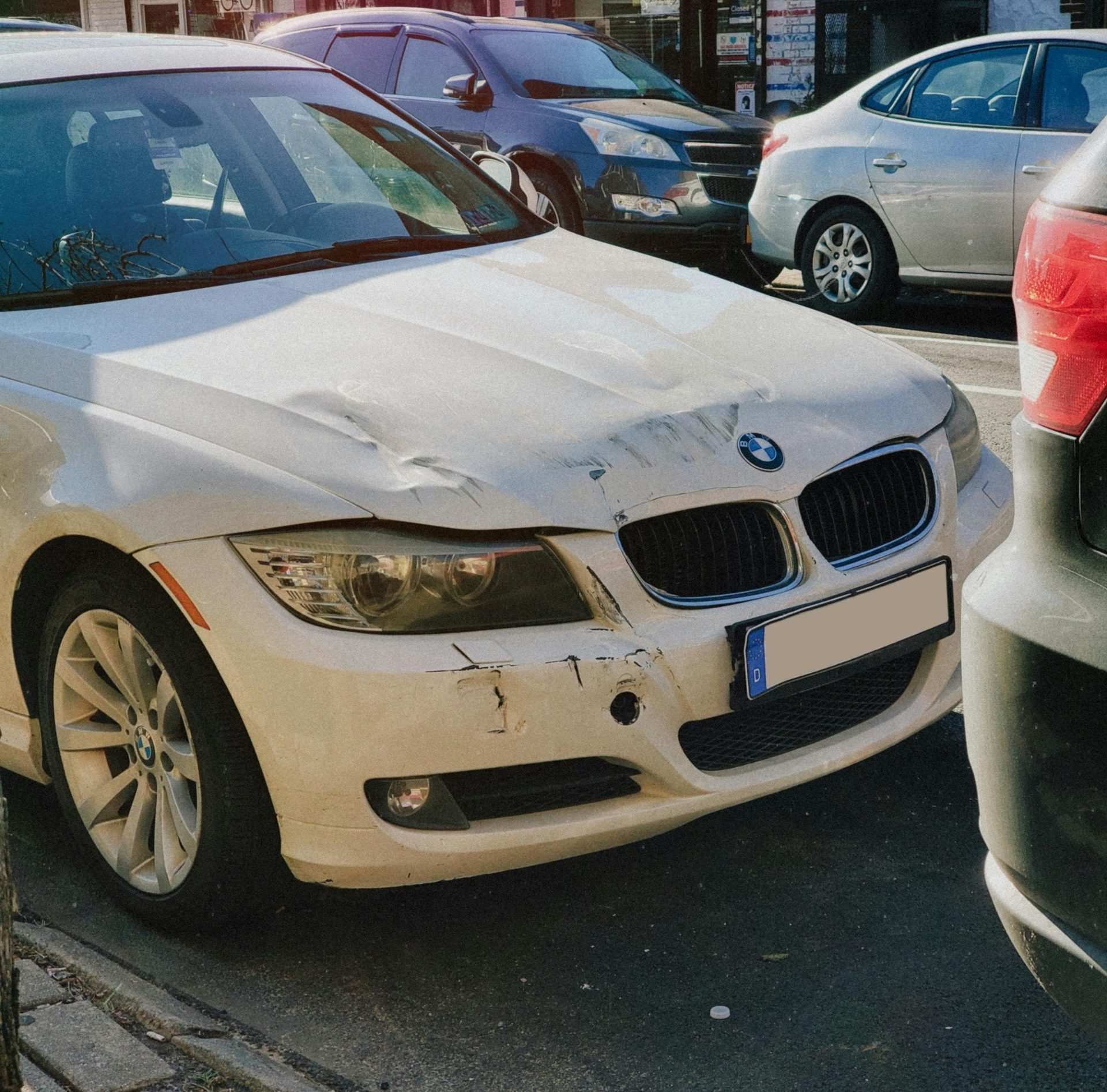White BMW sedan with front-end damage parked on a busy city street.